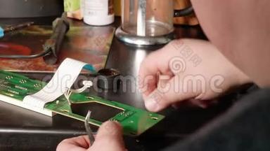 人的手的特写焊接电子卡。在家里，一个男人在脏餐桌上修理<strong>微波炉</strong>。
